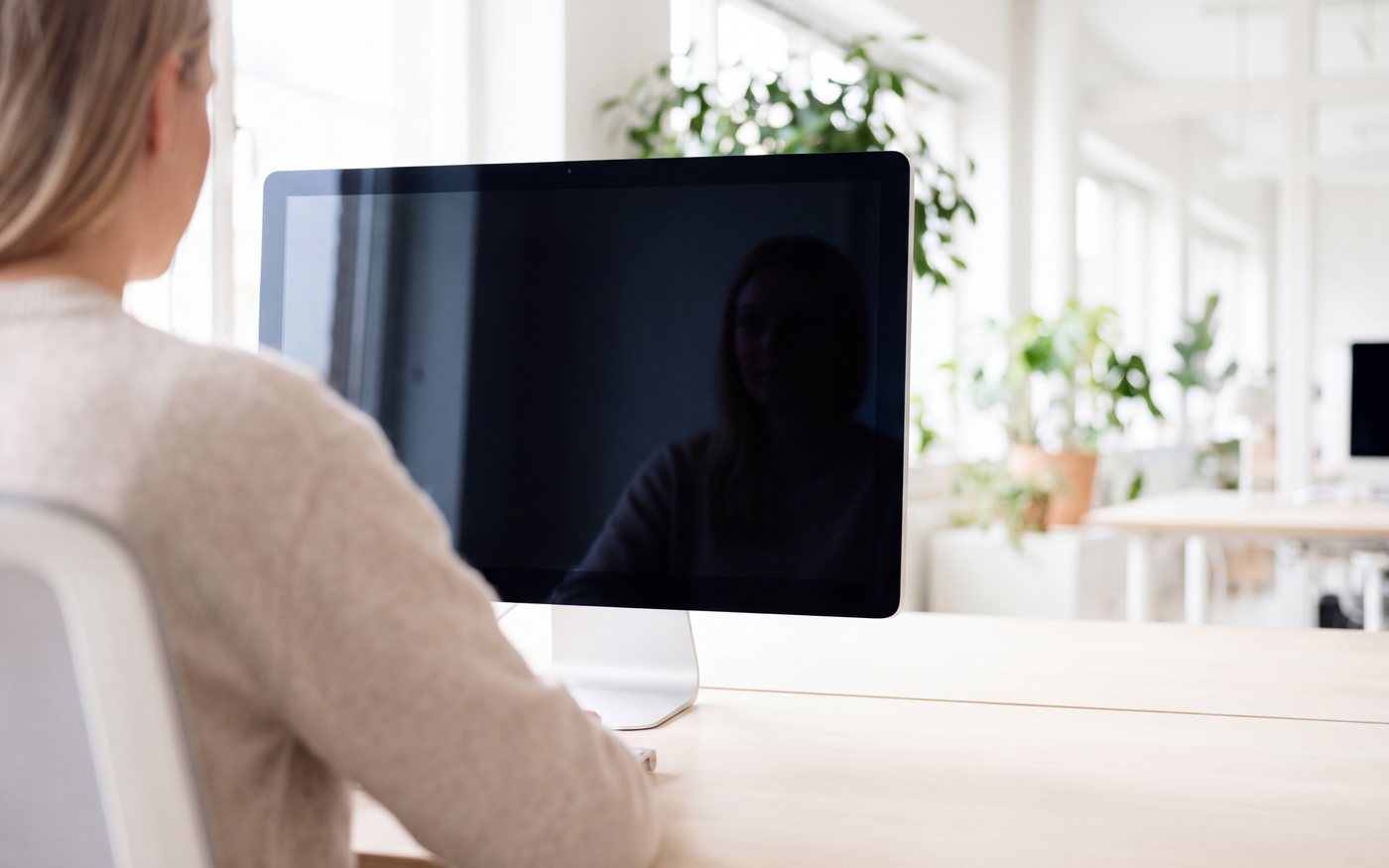 Over the shoulder of a person at a monitor in a sunlit open-plan office.