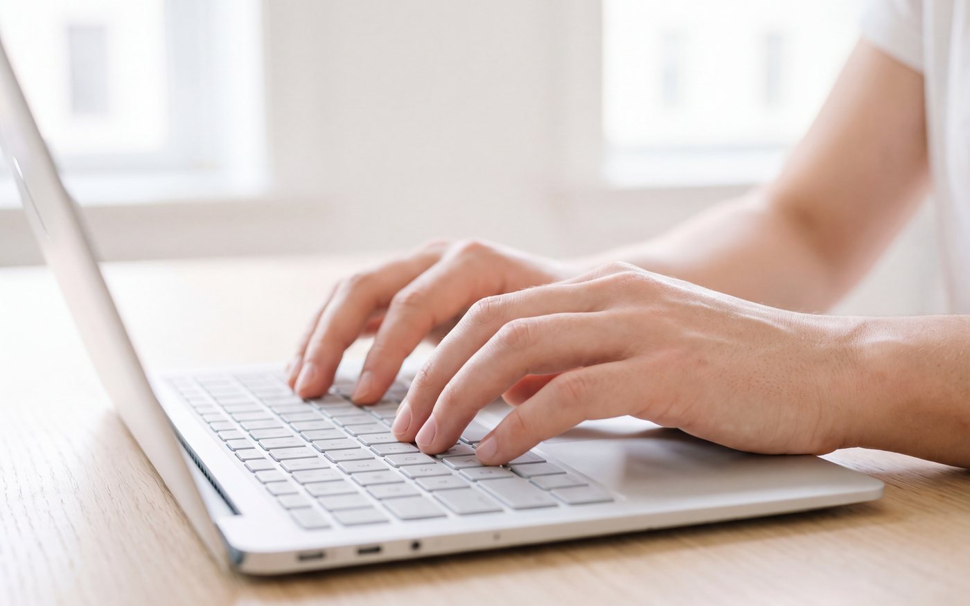 Fingers on a laptop keyboard in a bright office.